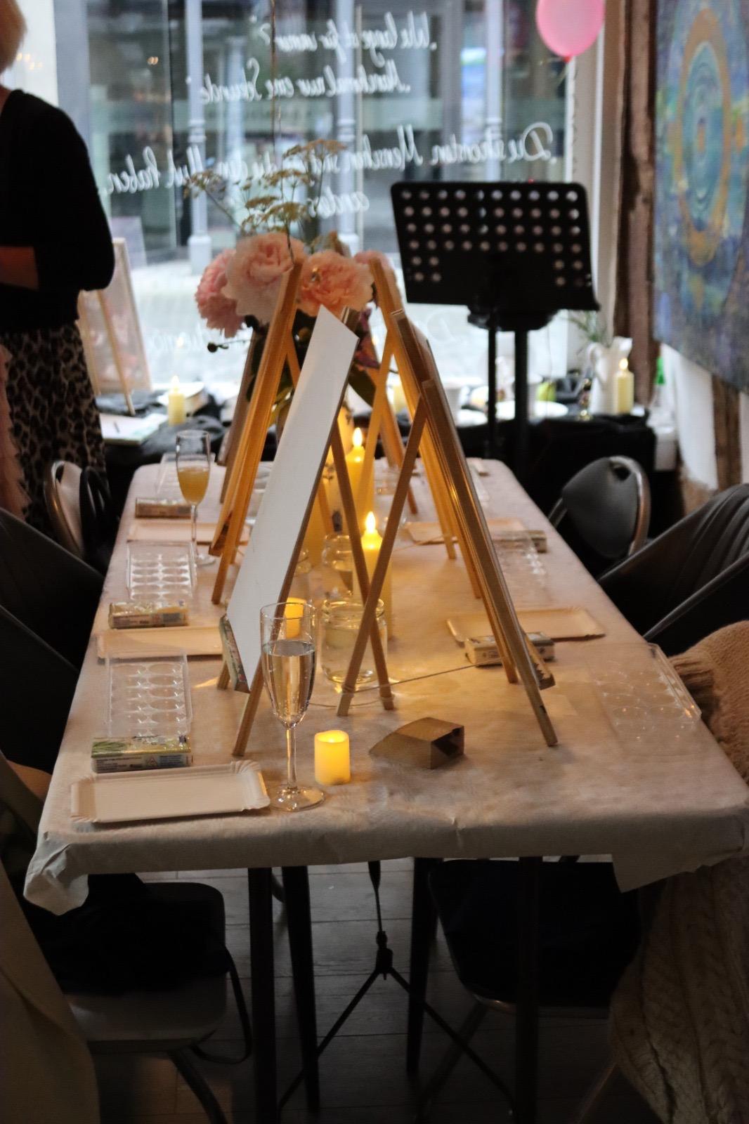 Gedeckter Tisch mit Staffeleien, Blumen und Kerzen bei einem Mal-Abend im Living Room